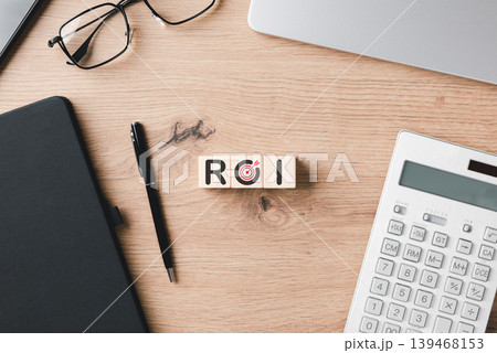 ROI return on investment concept featuring wooden blocks on an office desk with calculator and notebook to represent financial growth, profit analysis, and successful business goal marketing. 139468153