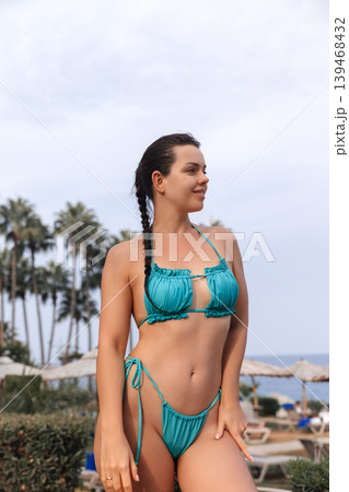 Beautiful woman posing confidently in turquoise bikini with glowing bronzed healthy summer complexion outdoors. Beautiful female showing smooth radiant body texture during tropical seaside resort 139468432