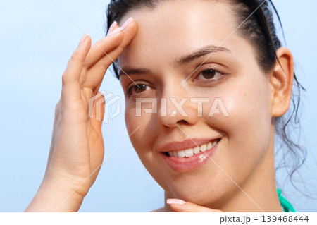 Young woman touching healthy facial skin with glowing smooth radiant complexion outdoors naturally today. Beautiful female showing fresh beauty texture during skincare routine beside tropical seaside 139468444