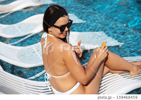 Beauty Female model using sunscreen bottle with radiant glowing smooth summer skin outdoors gracefully today. Beautiful female showing healthy bronzed texture during tropical poolside vacation near Beauty Female model using sunscreen bottle with radiant glowing smooth summer skin outdoors gracefully today. Beautiful female showing healthy bronzed texture during tropical poolside vacation near 139468459