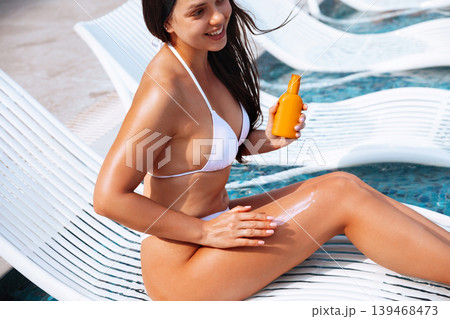 Beauty woman performing skincare routine with sunscreen lotion beside luxury swimming pool outdoors. Beautiful female applying sun cream and  showing smooth radiant legs  139468473