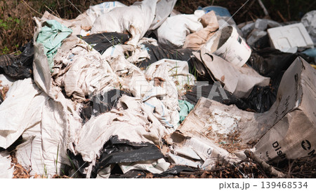 Piled Textile Waste And Plastic Sheeting, Torn Fabric, Synthetic Fibers And Tangled Bags Creating Choking Hazard For Undergrowth, Microfiber Shedding And Soil Smothering Visible In Close Detail Piled Textile Waste And Plastic Sheeting, Torn Fabric, Synthetic Fibers And Tangled Bags Creating Choking Hazard For Undergrowth, Microfiber Shedding And Soil Smothering Visible In Close Detail 139468534