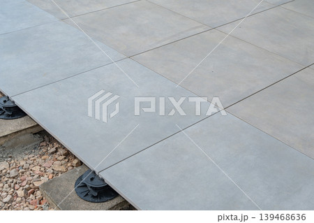Close-up of tile installation on adjustable supports. Ensures stability and proper drainage. Outdoor flooring system using large tiles and support base. Ideal for construction and architecture visuals Close-up of tile installation on adjustable supports. Ensures stability and proper drainage. Outdoor flooring system using large tiles and support base. Ideal for construction and architecture visuals 139468636