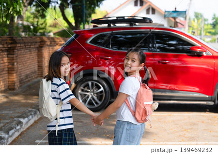 Two Asian student girls with backpacks holding hands and walking to the car to go home after school, Back to school and family transportation concept. Two Asian student girls with backpacks holding hands and walking to the car to go home after school, Back to school and family transportation concept. 139469232