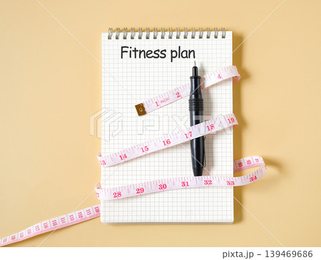 A measuring tape is wrapped around booknote with text FITNESS PLAN. A measuring tape is wrapped around booknote with text FITNESS PLAN. 139469686