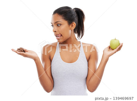 Woman, apple and chocolate in studio with diet risk, temptation and cheat day with healthy food choice or sugar in studio. Person with sweets versus green fruit in palm or detox on a white background 139469697
