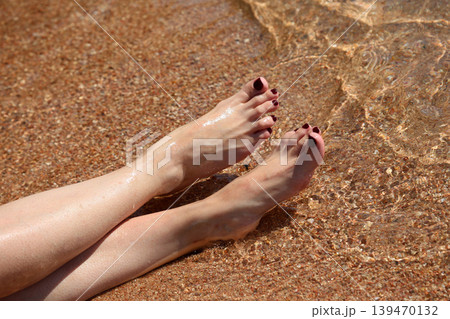 Women's feet with painted nails on the sand in clear sea water Women's feet with painted nails on the sand in clear sea water 139470132