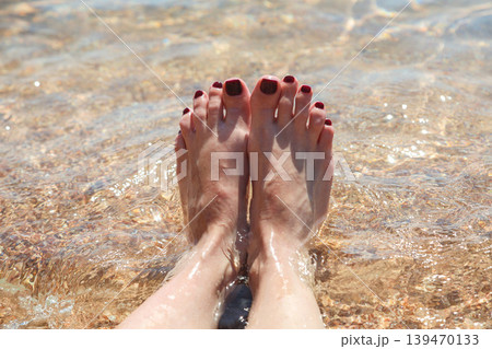 Women's feet with painted nails on the sand in clear sea water 139470133