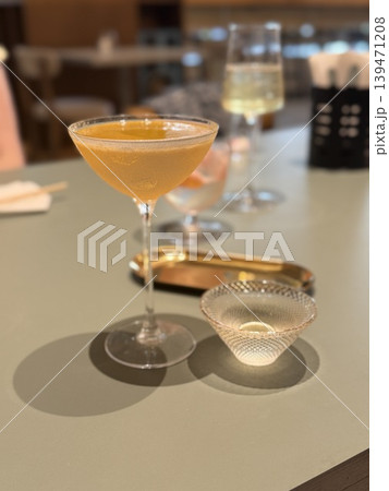 Cocktail glass with an amber drink on table with other drinks and bar setting in background Cocktail glass with an amber drink on table with other drinks and bar setting in background 139471208