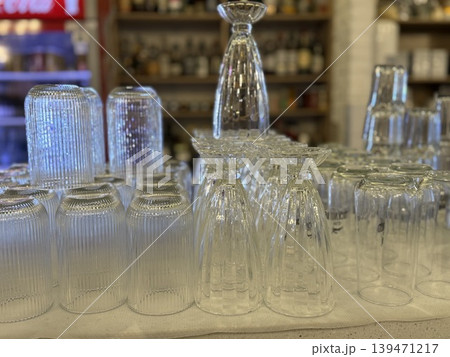 Upside-down glassware set on shelf in bar or restaurant with various drink bottles in background Upside-down glassware set on shelf in bar or restaurant with various drink bottles in background 139471217
