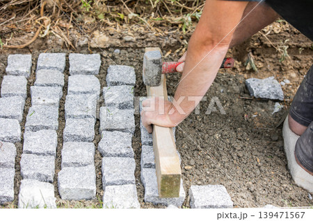Worker aligning cobblestone paving stones with hammer Worker aligning cobblestone paving stones with hammer 139471567