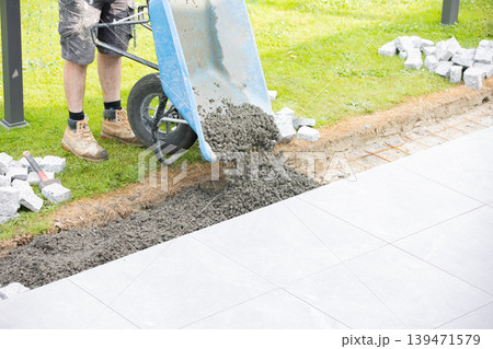 Construction worker pouring concrete from wheelbarrow for pavement installation Construction worker pouring concrete from wheelbarrow for pavement installation 139471579