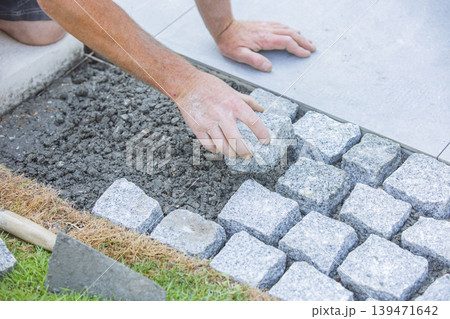 Worker placing cobblestone pavement by hand during installation Worker placing cobblestone pavement by hand during installation 139471642
