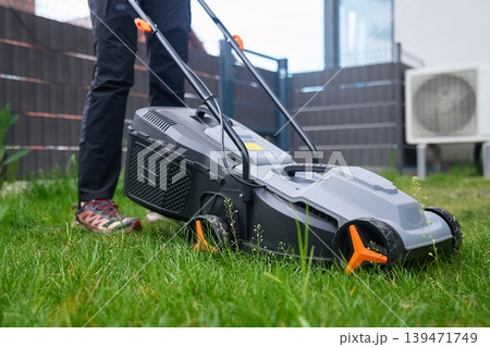 Lawn mower with grass collector stands in backyard grass near person Lawn mower with grass collector stands in backyard grass near person 139471749