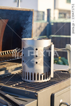 Charcoal chimney starter releases smoke while standing on an outdoor grill grate Charcoal chimney starter releases smoke while standing on an outdoor grill grate 139471751