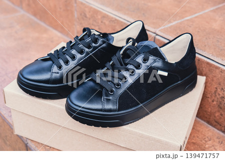 Elegant black leather womens shoes blank product for branding displayed on recycled cardboard box. New casual female sneakers no-brand footwear e-commerce. No logo product Elegant black leather womens shoes blank product for branding displayed on recycled cardboard box. New casual female sneakers no-brand footwear e-commerce. No logo product 139471757