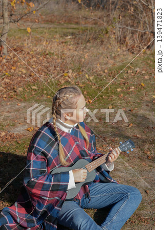 Blonde woman playing guitar ukulele outdoors in autumn forest. Concept of sound therapy, mental health and wellness rituals. Calmness tranquility audio-sensory practices. Aura farming Blonde woman playing guitar ukulele outdoors in autumn forest. Concept of sound therapy, mental health and wellness rituals. Calmness tranquility audio-sensory practices. Aura farming 139471823