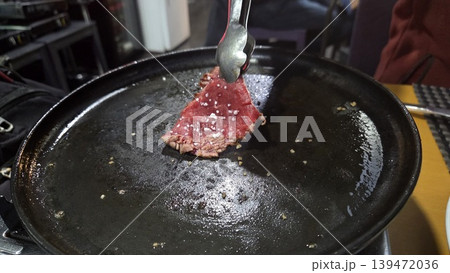 Thin beef slice sizzling on a hot cast iron griddle in a spanish restaurant for food background and menu banner design Thin beef slice sizzling on a hot cast iron griddle in a spanish restaurant for food background and menu banner design 139472036