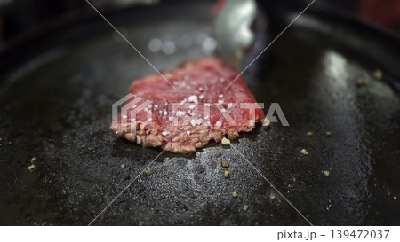 Close up thin beef slice cooking on a black hot griddle with coarse salt for food detail background and menu photography use Close up thin beef slice cooking on a black hot griddle with coarse salt for food detail background and menu photography use 139472037