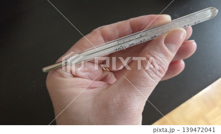 Hand holding glass mercury clinical thermometer for medical illustration and patient care banner design 139472041