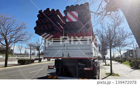 Rear view of a truck carrying stacked red pipes on city road for road repair and infrastructure transport background 139472078