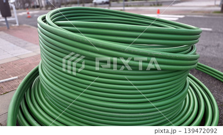 Closeup of tightly coiled green conduit showing texture and spiral pattern for industrial installation or material detail background and technical documentation. Telecommunication pipes Closeup of tightly coiled green conduit showing texture and spiral pattern for industrial installation or material detail background and technical documentation. Telecommunication pipes 139472092