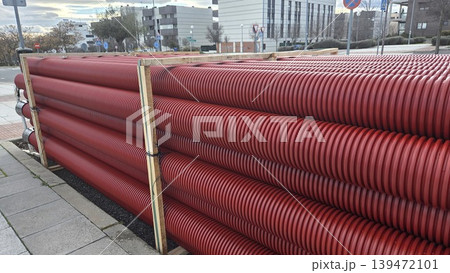 Long rows of red corrugated drainage pipes strapped in wooden frames for road repair and public works supply background and construction banner Long rows of red corrugated drainage pipes strapped in wooden frames for road repair and public works supply background and construction banner 139472101
