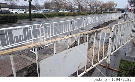 Fenced urban trench along roadside for pipe laying and road repair with pedestrian barrier for construction documentation and safety banner use Fenced urban trench along roadside for pipe laying and road repair with pedestrian barrier for construction documentation and safety banner use 139472185