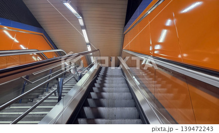 Escalator leading up through modern madrid metro station with orange tiled walls and stainless steel handrails for transport background and architecture poster Escalator leading up through modern madrid metro station with orange tiled walls and stainless steel handrails for transport background and architecture poster 139472243