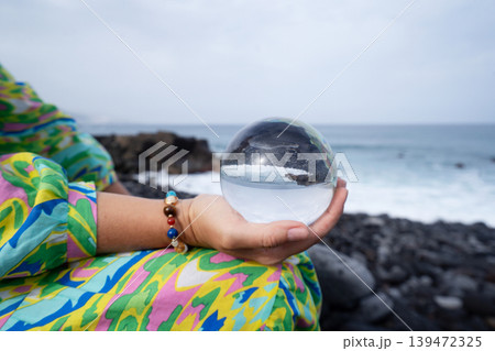 woman meditating on beach shore and holding crystal ball 139472325