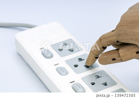 Wooden Articulated Mannequin Hand with Finger Inserting into Dangerous Electrical Outlet Socket on White Power Strip, Electricity Hazard Concept 139472385