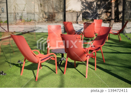 Modern red lounge chairs arranged around a table on artificial green grass in a bright outdoor patio area. 139472411