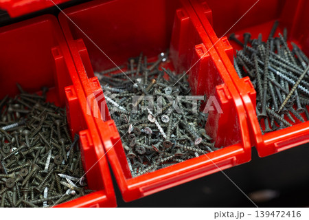Various metal screws organized in red plastic storage bins in a workshop, close-up view. Various metal screws organized in red plastic storage bins in a workshop, close-up view. 139472416