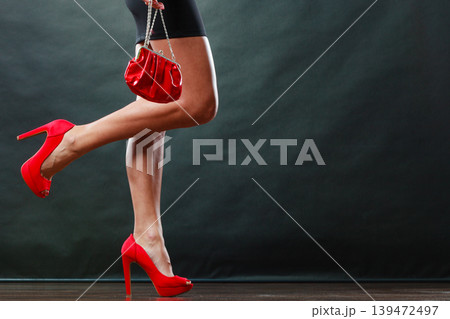 Girl in black short dress red spiked shoes holds handbag 139472497