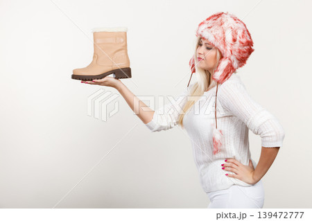 Woman in winter hat holding beige boots. 139472777