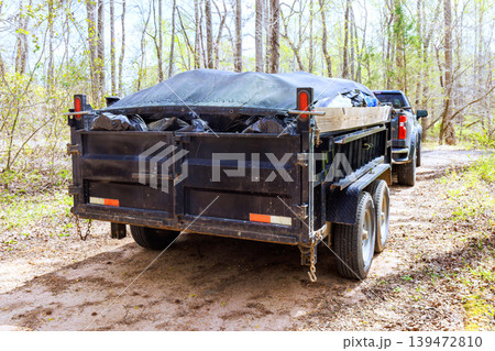 Dump trailer to garbage is parked on dirt road surrounded by trees 139472810