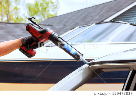 Worker uses caulking gun to apply sealant on car roof near parked boat Worker uses caulking gun to apply sealant on car roof near parked boat 139472837