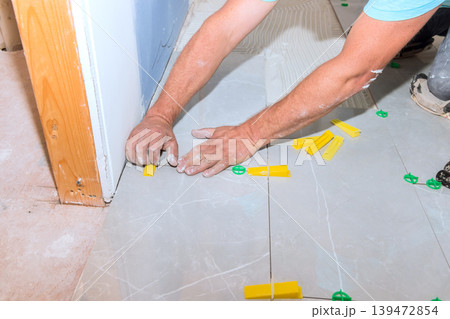 Tiler worker lays tiles on floor using spacers tools in construction setting 139472854