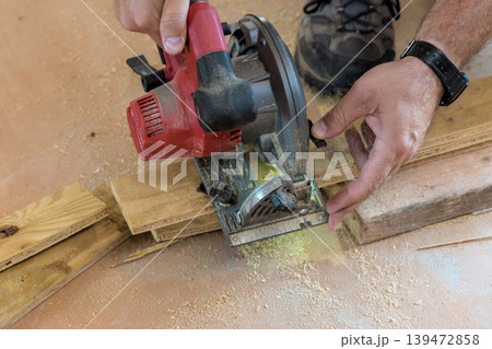 Carpenter is cutting wooden boards with circular saw on flat surface inside contractor area workshop. Carpenter is cutting wooden boards with circular saw on flat surface inside contractor area workshop. 139472858