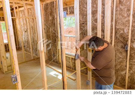 Worker uses measuring tool to mark wooden studs inside house progress in construction site. Worker uses measuring tool to mark wooden studs inside house progress in construction site. 139472883