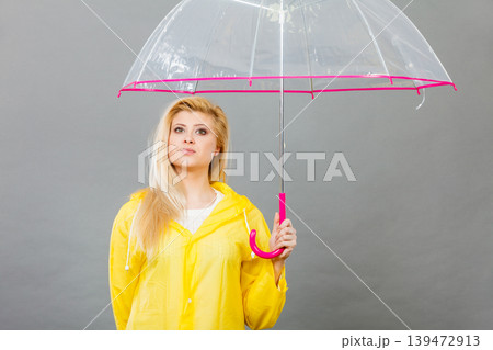 Sad bored woman wearing raincoat holding umbrella 139472913