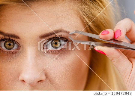 Woman tweezing eyebrows depilating with tweezers Woman tweezing eyebrows depilating with tweezers 139472948