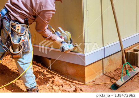 Worker using nail gun to attach panels on building site to materials to foundation Worker using nail gun to attach panels on building site to materials to foundation 139472962