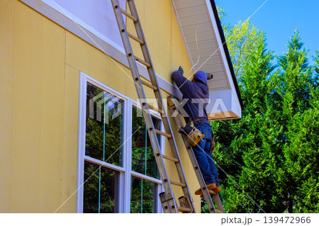 Handyman is installing siding exterior of yellow house by climbing ladder Handyman is installing siding exterior of yellow house by climbing ladder 139472966