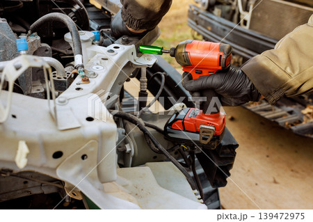 Car worker holds cordless drill to fix parts of vehicle metal frame in workshop outside 139472975