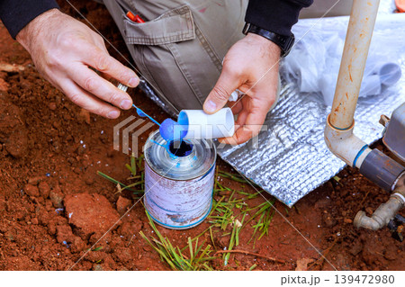 Worker stands in dirt, using adhesive blue glue of plastic pipe with water PVC Worker stands in dirt, using adhesive blue glue of plastic pipe with water PVC 139472980