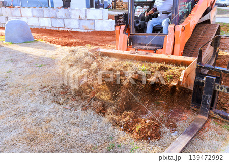 Worker operates machine to remove dirt debris from yard in residential area during landscaping work 139472992