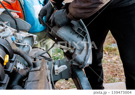Worker are working on car headlight one is removing part while others observe assist in garage. 139473004