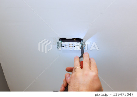 Handyman is installing an electrical outlet in wall they are using screwdriver to secure it in place 139473047