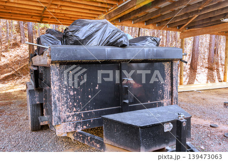 Garbage truck parked under wooden shelter filled with black trash bags in wooded area Garbage truck parked under wooden shelter filled with black trash bags in wooded area 139473063